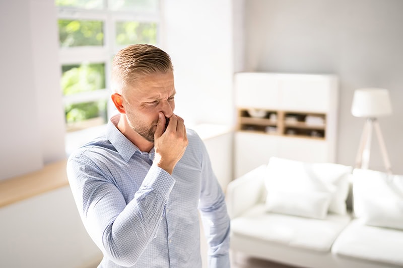 A man standing in his home plugging his nose because he smells something stinky