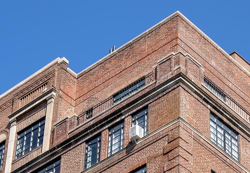 Upper corner of a classic red-brick building facade against a clear, bright blue sky.