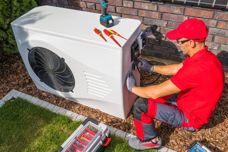 A handyman in a red shirt repairing a heat pump